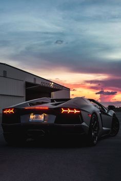 a black sports car parked in front of a building with the sun setting behind it