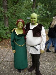 two people in costumes standing next to each other on a sidewalk with trees behind them