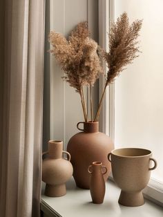 three vases are sitting on a window sill with some dried plants in them