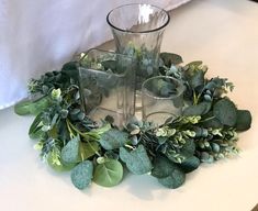 there is a glass vase with some plants in it on the table next to two glasses