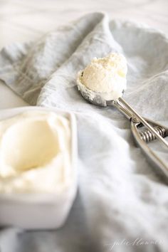 a spoon with ice cream sitting on top of a white plate next to an empty container