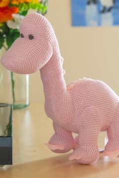 a knitted pink dinosaur toy sitting on top of a table next to a vase filled with flowers