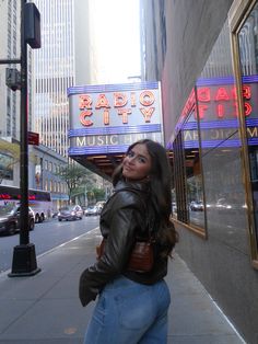 a woman standing on the sidewalk in front of a radio city music hall sign and building