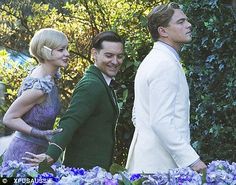 two men and a woman standing next to each other in front of some bushes with trees behind them