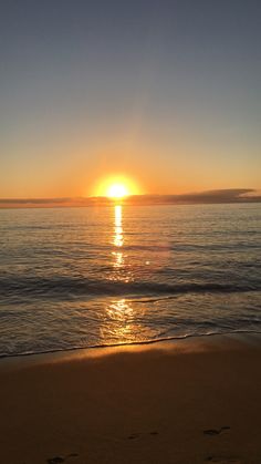 the sun is setting over the ocean with footprints in the sand