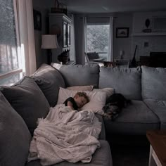 a woman laying on top of a couch next to a dog