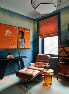 a living room with an orange chair and two paintings on the wall behind it,