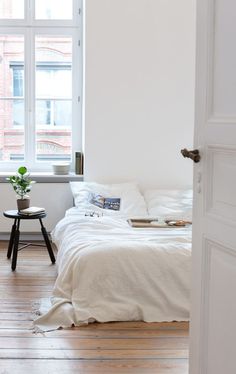 an open door leading to a bedroom with white walls and wood floors, along with a bed in the corner