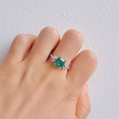 Few color schemes have a more sophisticated and luxurious feel than the iconic pairing between silver and emerald green – and this is a style we’ve captured in our stunning Ivy ring design. Simplistic yet beautiful, our Emerald ivy ring features a massive, 2.0-carat emerald as the main center, while six striking CZ crystals transform the look and create an unrivaled level of sophistication overall. ✦ DETAILS ✦✧ Handcrafted ✧ 2.0 Carat center stone✧ Emerald and cz crystals ✧ Sizes 3.75-11.25✧ Thi Emerald Cut May Birthstone Crystal Ring, Elegant Open Emerald Ring With Cubic Zirconia, Elegant White Gold Crystal Ring For May Birthstone, Green Ring For Proposal, Green Emerald Jewelry For Proposal, Elegant Emerald Promise Ring, Green Jewelry For Proposal, Green Solitaire Jewelry For Proposal, Green Emerald Cut Birthstone Ring