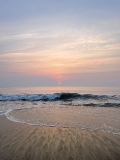 the sun is setting over the ocean with waves coming in from the water and sand on the beach