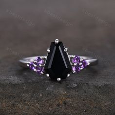 a black diamond ring with amethyst purple stones on the sides, set in white gold