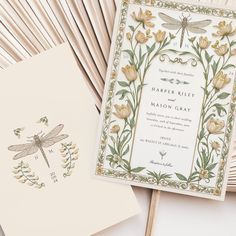 the wedding stationery is laid out on top of each other, with dragonflys and flowers