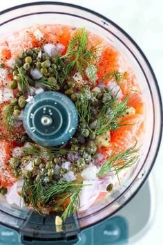 an overhead view of a food processor with vegetables and seasonings in it on a white surface