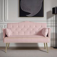 a pink couch sitting in front of a painting on the wall next to a lamp