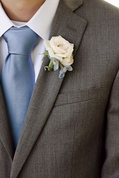 a man wearing a gray suit with a blue tie and white rose boutonniere