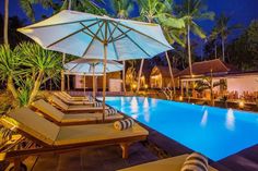 an outdoor swimming pool with lounge chairs and umbrellas next to it at night time