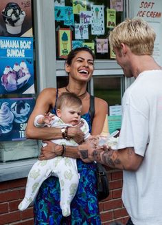 a man holding a baby in his arms while standing next to a woman with tattoos on her arm