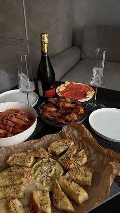 a table topped with plates and bowls filled with food next to bottles of wine on top of a couch