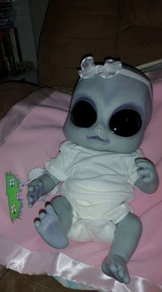 a baby alien doll sitting on top of a pink blanket