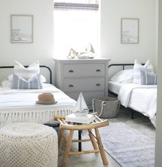 two beds in a bedroom with white linens and pillows on the bed, along with a small stool