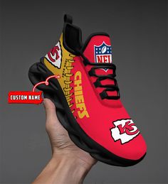 a hand holding up a red and yellow sneaker with the nfl logo on it