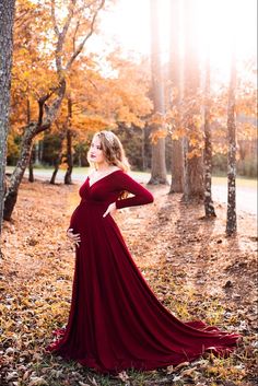 a pregnant woman in a long red dress standing next to a tree