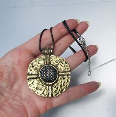 "This fabulous and eye-catching 1980s vintage black neck cord necklace has a large 2\" wide round hammered antiqued gold-tone pendant with a gorgeous Etruscan Revival design.  It's center has amazing black and blue aurora borealis rhinestones that have brilliant gold sparkle.  The black neck cord is 18\" long plus it has a 2\" extender chain.  The back of the pendant looks like it has wear, but it feels smooth and solid so I think it was made that way to look antique.  It is in excellent conditi Black Metal Necklace With Antique Finish, Black Metal Jewelry With Antique Finish, Black Metal Medallion Jewelry, Black Medallion Metal Jewelry, Adjustable Metal Medallion Necklace, Black Metal Medallion Necklace, Round Metal Medallion Necklace With Large Pendant, Revival Design, Blue Aurora