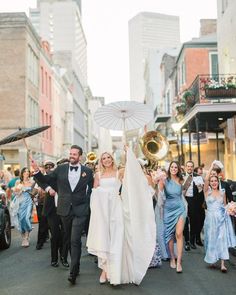 a bride and groom walking down the street with their wedding party in the background holding an umbrella