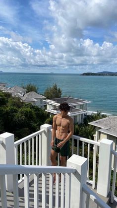 a shirtless man standing on a balcony next to the ocean