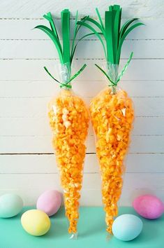 two carrots with plastic wrappers on them sitting in front of some colored eggs