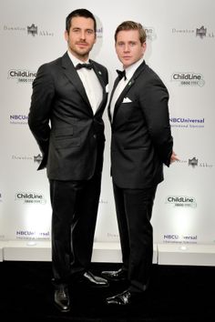 two men in tuxedos standing next to each other on a black carpeted floor