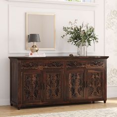 a wooden sideboard with carvings on it and a vase filled with flowers next to it