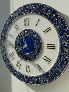 a blue and white clock with roman numerals on it's face hanging from the wall