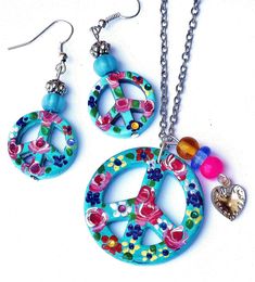 "A Boho necklace featuring a turquoise blue peace sign pendant that's covered in colorful painted flowers in pink, yellow, and purple, with sparkling Swarovski crystal rhinestone accents! Dangling alongside the artful pendant, a little silver heart charm and glass lampwork beads add fun movement! Just choose your chain length to add this super-cute piece of Boho-style wearable art to your collection! Ceramic Pendant 1 1/4\" round, Silver-plated Necklace w/ Lobster Clasp 18\"-28\", Silver-plated Peace Sign Jewelry For Gifts, Hippie Multicolor Nickel-free Jewelry, Pink Hippie Jewelry For Gift, Pink Hippie Jewelry For Gifts, Pink Hippie Style Jewelry For Gift, Peace Necklace, Peace Sign Necklace, Sign Necklace, Glass Lampwork