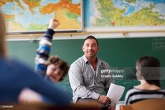 a man sitting in front of a blackboard with his hand up to the sky