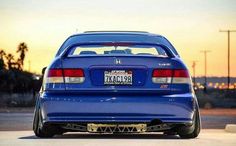 the back end of a blue car parked in a parking lot at sunset or dawn