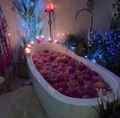 a bathtub filled with lots of flowers in a bathroom next to plants and candles