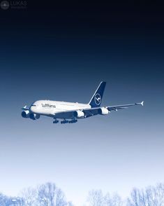 an airplane is flying in the sky with trees behind it and snow on the ground