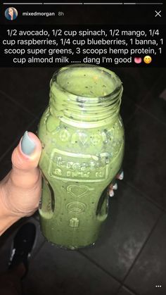 a person holding up a green drink in a mason jar