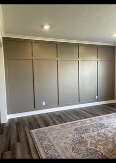 an empty living room with gray walls and wood flooring on the far wall is a rug