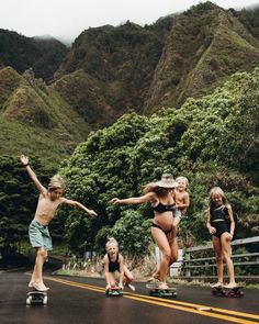 two girls and one boy are skateboarding down the road with mountains in the background