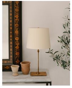 a lamp on a table next to a mirror and potted plant in front of it