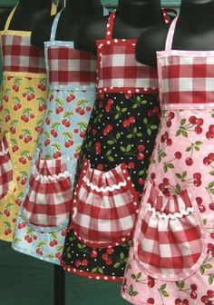 several aprons hanging on a rack in front of a green wall with red and white checkered fabric