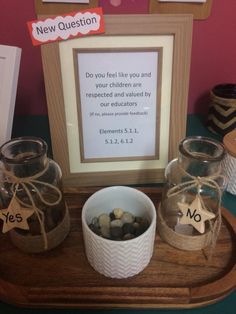 a wooden tray topped with glass jars filled with rocks and pebbles next to a framed sign