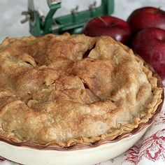 an apple pie sitting on top of a white plate next to some red and green apples