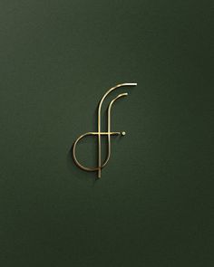 the letter f is made out of gold wire and sits on a dark green surface