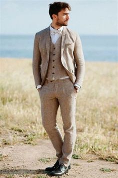 a man wearing a suit and tie standing on a dirt road next to the ocean