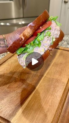 a person holding up a sandwich with meat and lettuce in it on a cutting board