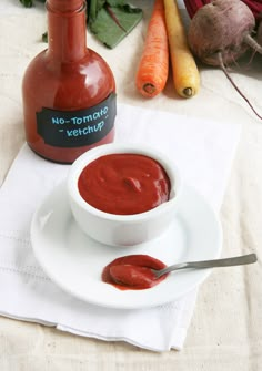 a white plate topped with a bowl of sauce next to carrots and a bottle of ketchup