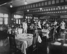 an old black and white photo of people in a dining room with tables set for dinner